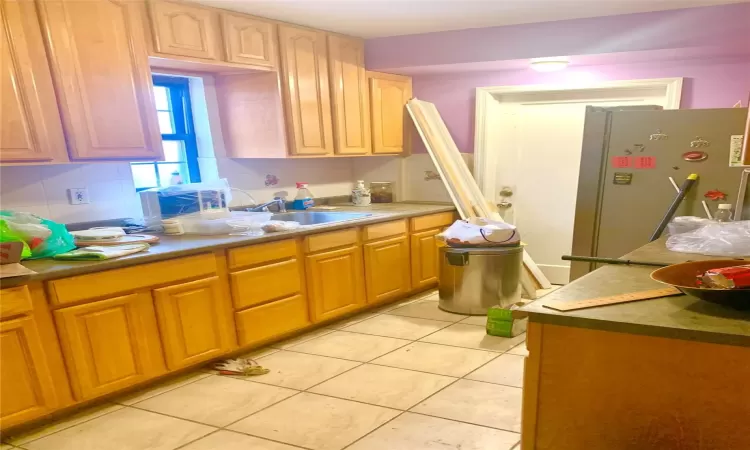 Kitchen with backsplash, light tile patterned floors, freestanding refrigerator, and a sink