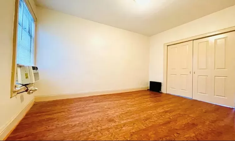 Unfurnished bedroom with cooling unit, wood finished floors, baseboards, and a closet