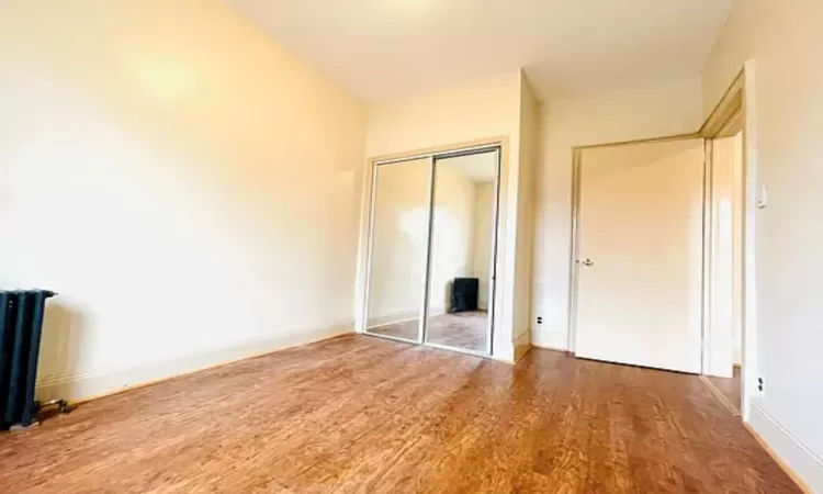 Unfurnished bedroom featuring a closet, baseboards, radiator, and wood finished floors