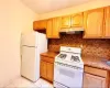 Kitchen with under cabinet range hood, stone countertops, tasteful backsplash, white appliances, and light tile patterned floors