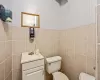 Half bathroom with vanity, tile walls, and toilet