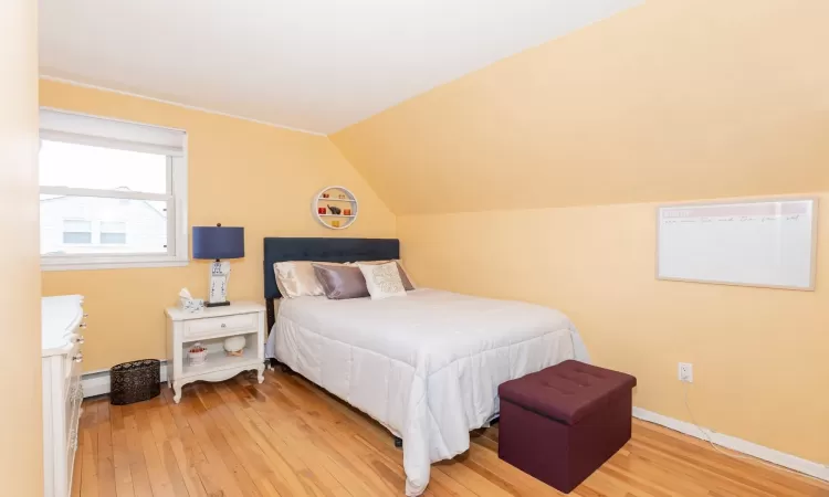 Bedroom featuring a baseboard radiator, light wood-type flooring, baseboards, and vaulted ceiling