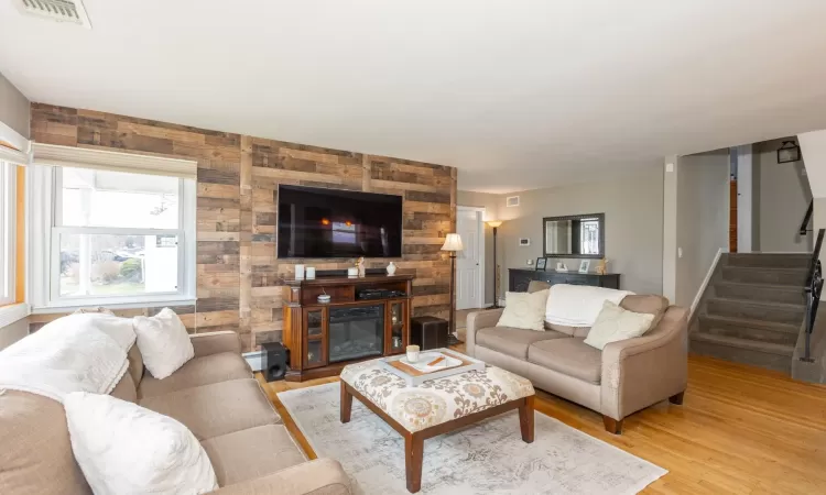 Living room with visible vents, light wood-style flooring, baseboard heating, and stairs