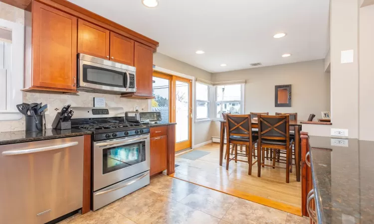 Kitchen with decorative backsplash, brown cabinets, appliances with stainless steel finishes, and dark stone counters