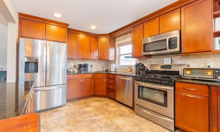 Kitchen featuring brown cabinetry, a toaster, a sink, appliances with stainless steel finishes, and tasteful backsplash