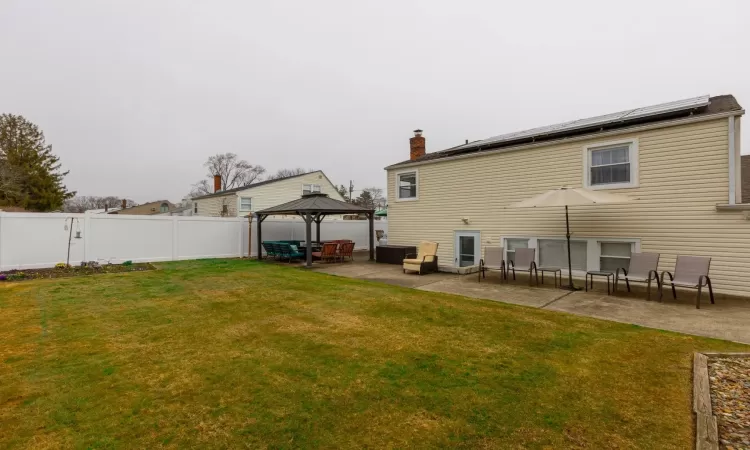 Rear view of house with a lawn, roof mounted solar panels, a fenced backyard, a gazebo, and a patio area