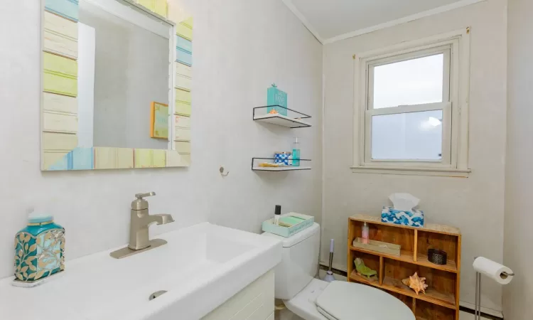 Bathroom featuring a sink, a baseboard heating unit, toilet, and crown molding