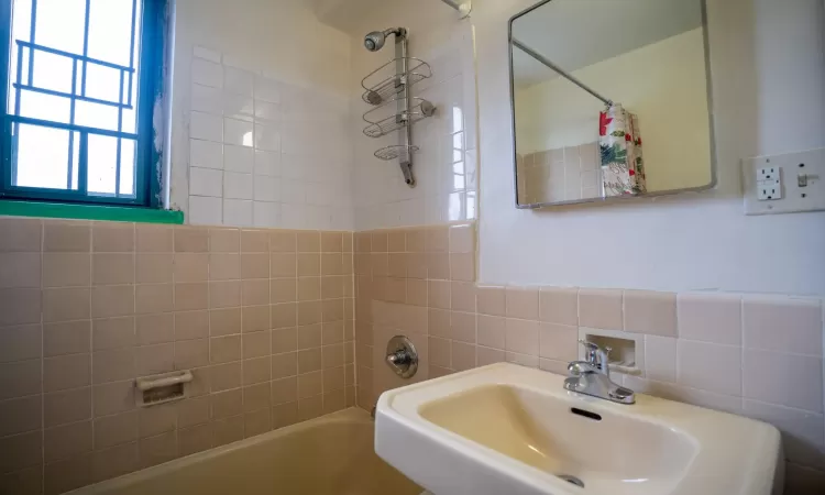 Bathroom featuring tile walls, shower / tub combo with curtain, and a sink