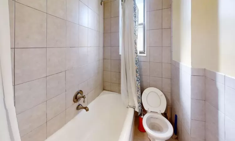 Bathroom with toilet, tile walls, and shower / tub combo with curtain