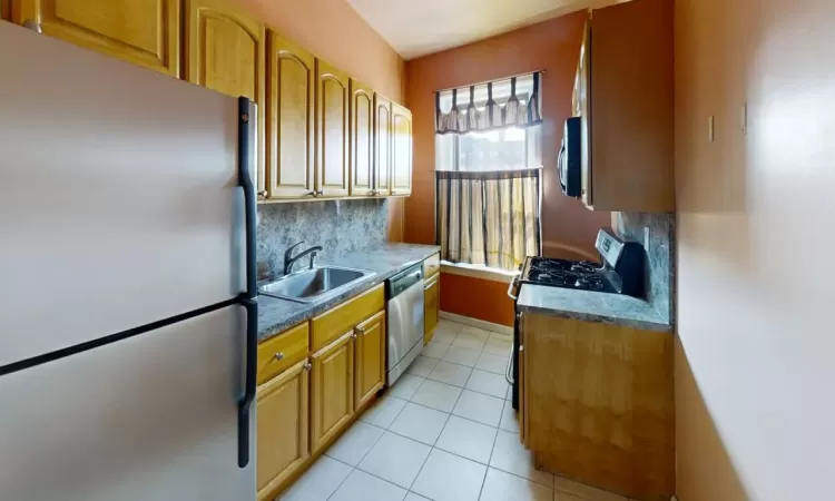 Kitchen featuring baseboards, light tile patterned flooring, a sink, stainless steel appliances, and backsplash