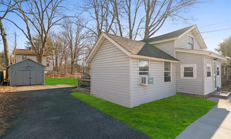 View of home's exterior with a yard, an outbuilding, a storage shed, and a shingled roof