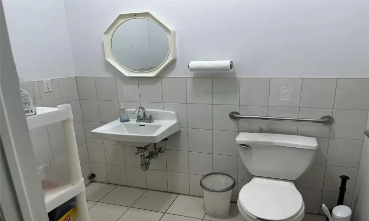 Half bath with tile patterned flooring, toilet, a wainscoted wall, and a sink